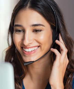 Smiling woman using laptop while talking to customer on phone. Consulting corporate client in conversation with customer using computer on desk. Service desk consultant talking in a call center and working on laptop.