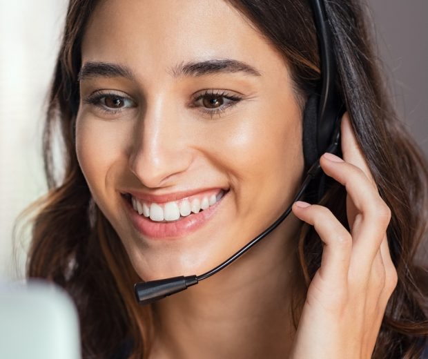 Smiling woman using laptop while talking to customer on phone. Consulting corporate client in conversation with customer using computer on desk. Service desk consultant talking in a call center and working on laptop.